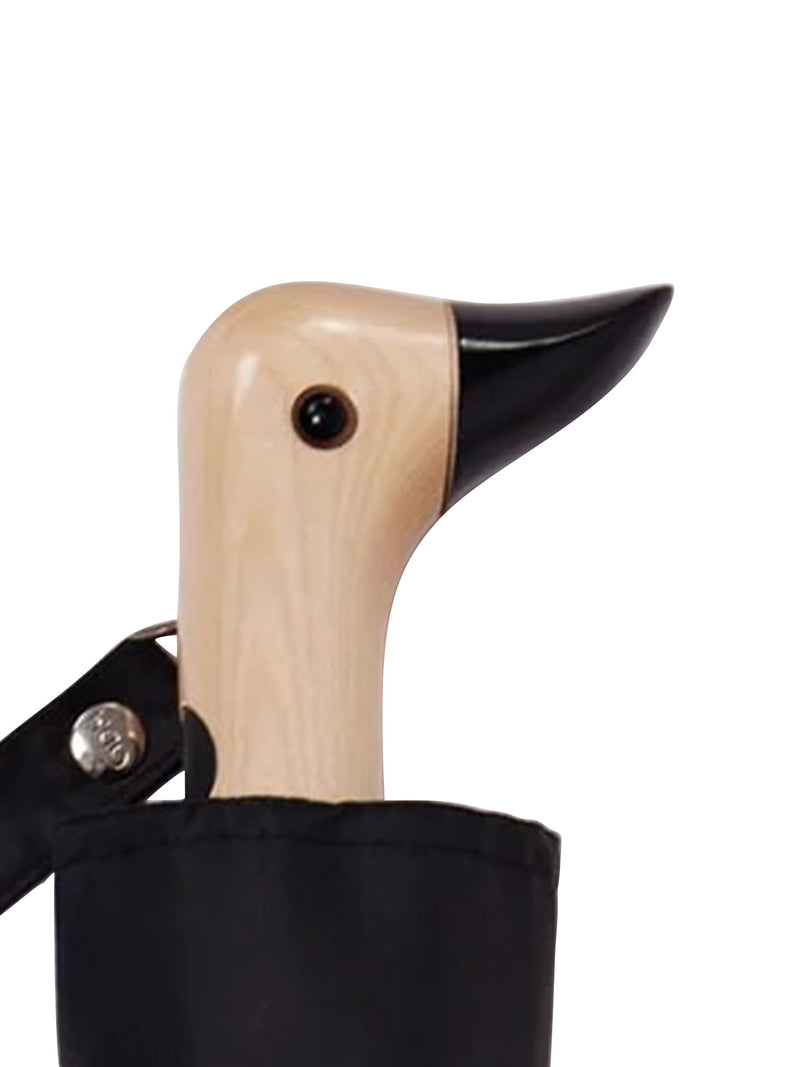 A close-up of a duck-shaped umbrella handle made of light natural wood with a glossy black beak and eye detail looking straight to the camera its' beak raised up, emerging from a black fabric sleeve on a white background.
