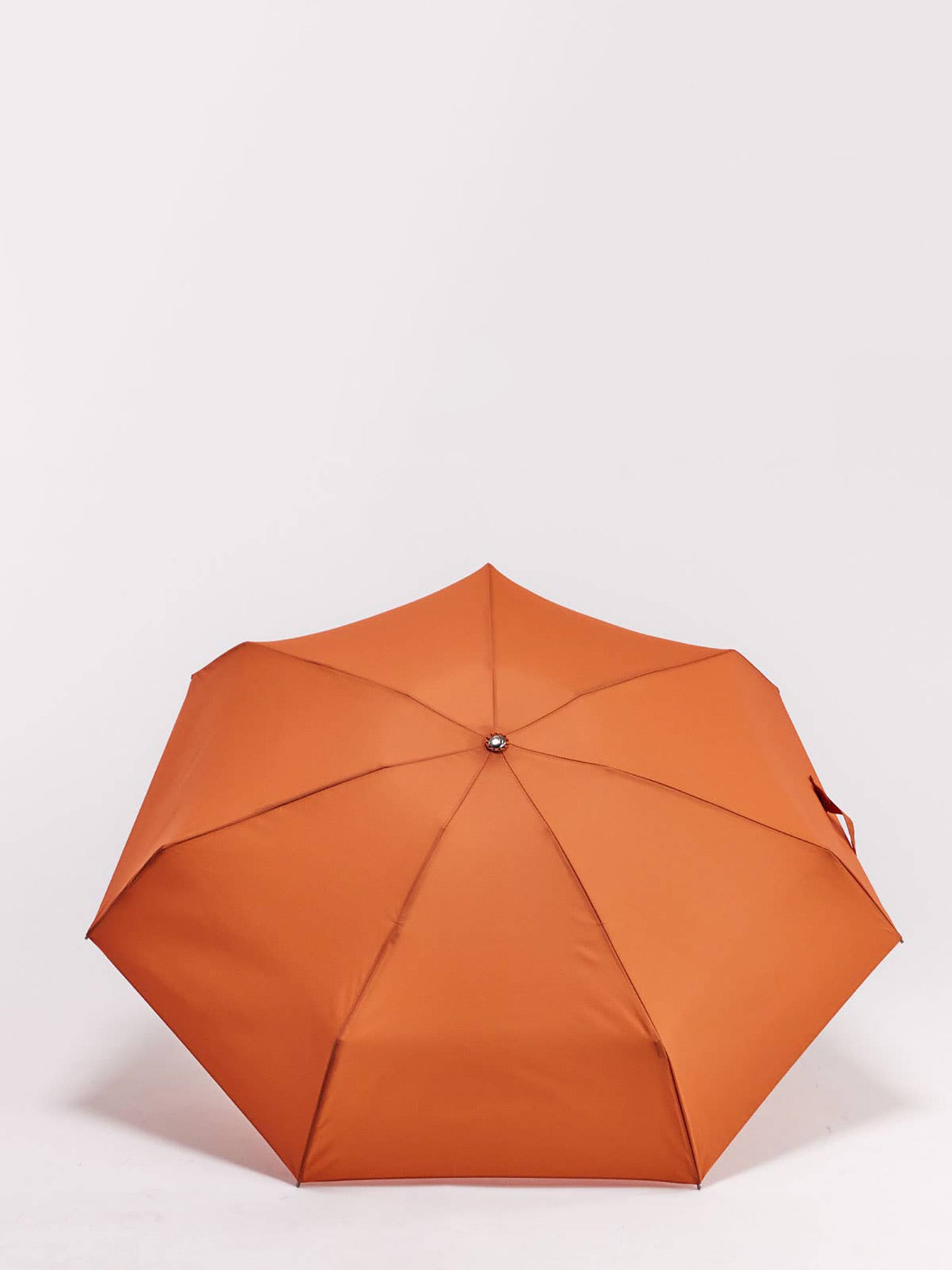 An orange compact umbrella shown open from a top-down view on a clean white background.