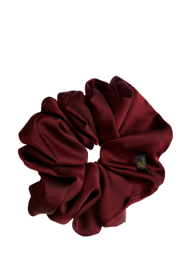 A deep burgundy red satin hair scrunchie with a small black and gold brand tag, shown on a solid white background.