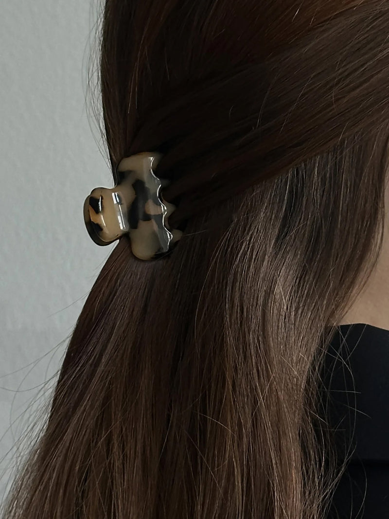 A close-up of a person's dark brown hair secured partly on their neck with a tortoiseshell hair claw clip against a light gray wall.