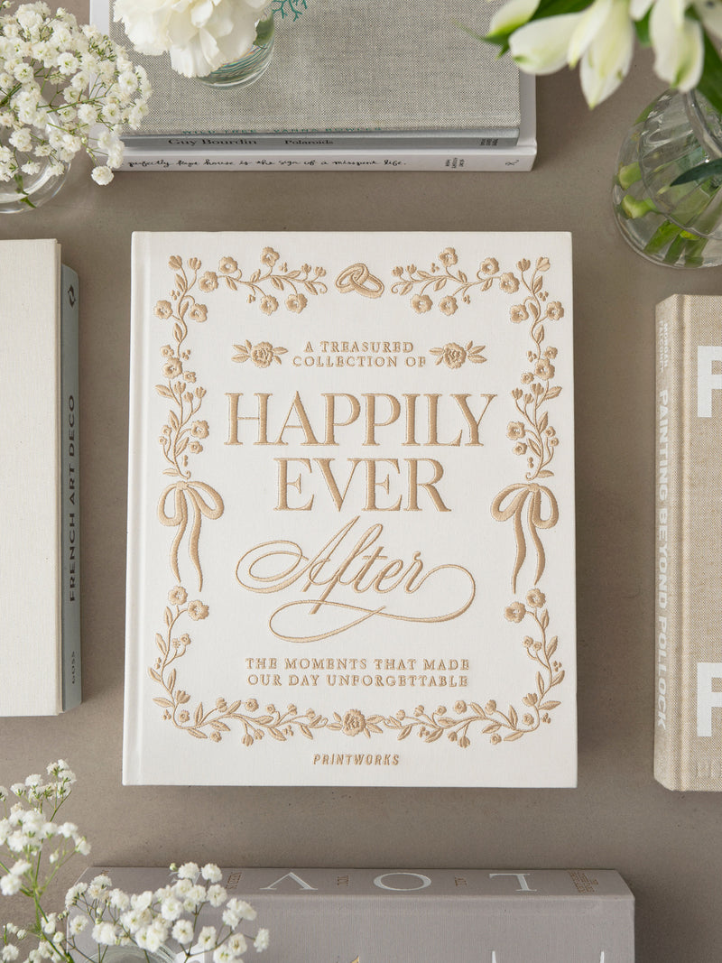 Photo album 'Happily Ever After' with decorative cover on a surface with flowers and books.