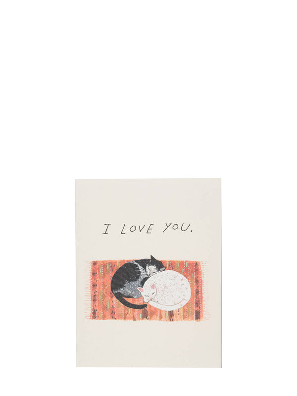 A square greeting card with the handwritten text 'I LOVE YOU.' above an illustration of a black-and-white cat curled with a white cat napping up on a textured orange-red blanket against a cream background.