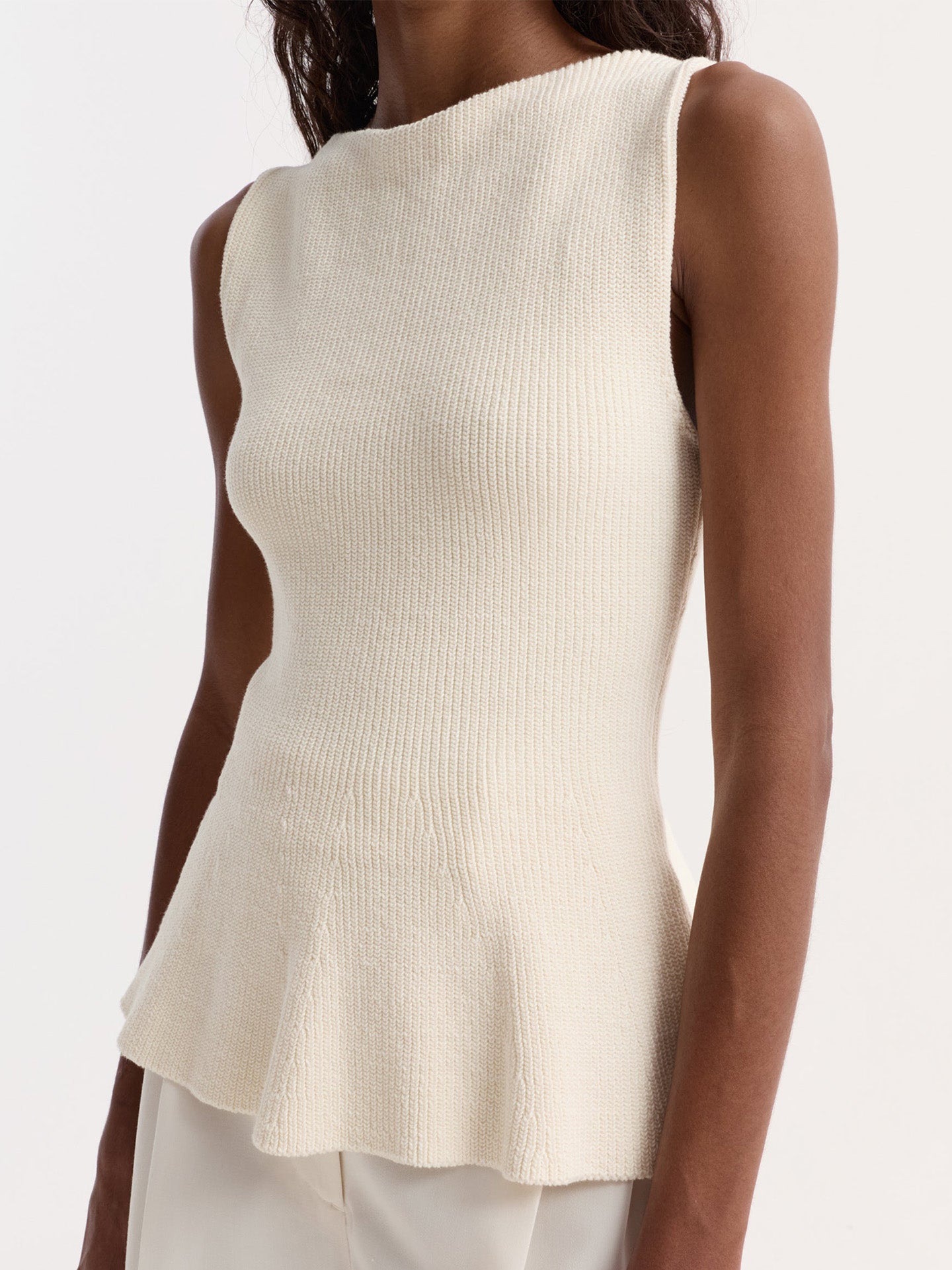 Woman wearing a cream ribbed sleeveless top against a white background