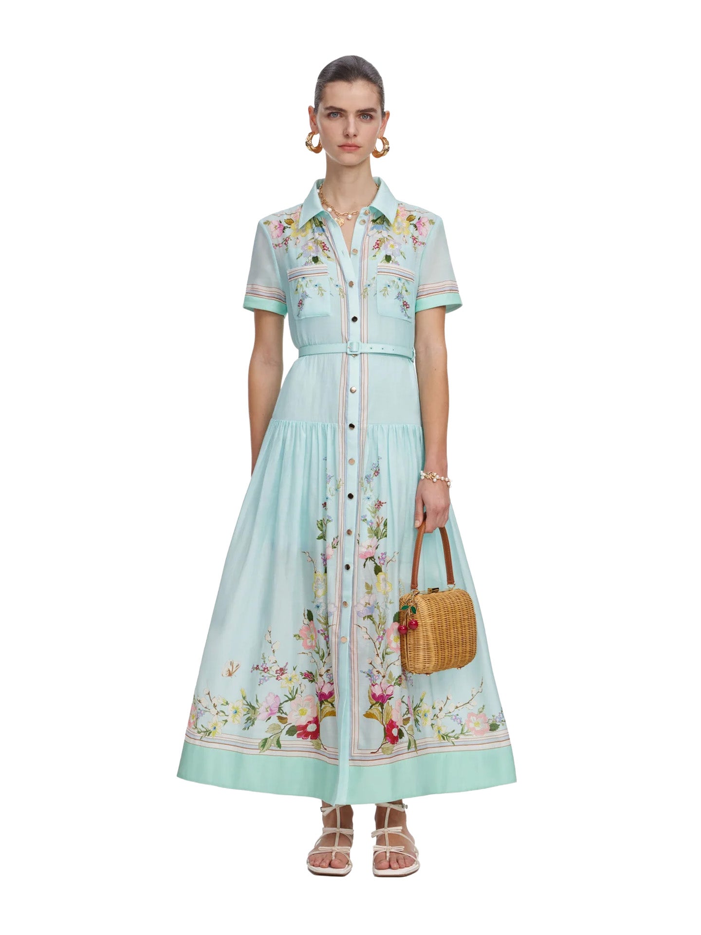 Woman wearing a light blue floral dress holding a woven bag on a white background