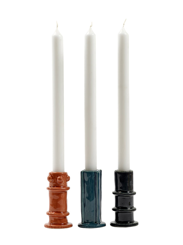 Three candles in different ceramic holders of different colors and shapes designed by Marie Michelsen on a white background