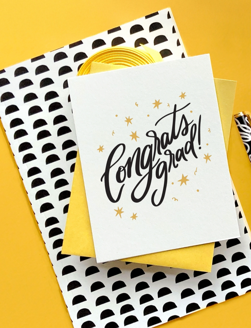 Graduation card with 'Congrats grad!' text on a patterned envelope against a yellow background