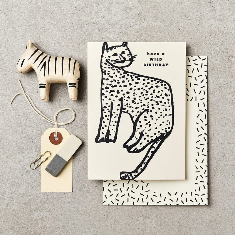 Card with a cat illustration and 'have a wild birthday' text, placed on a textured surface with decorative items.