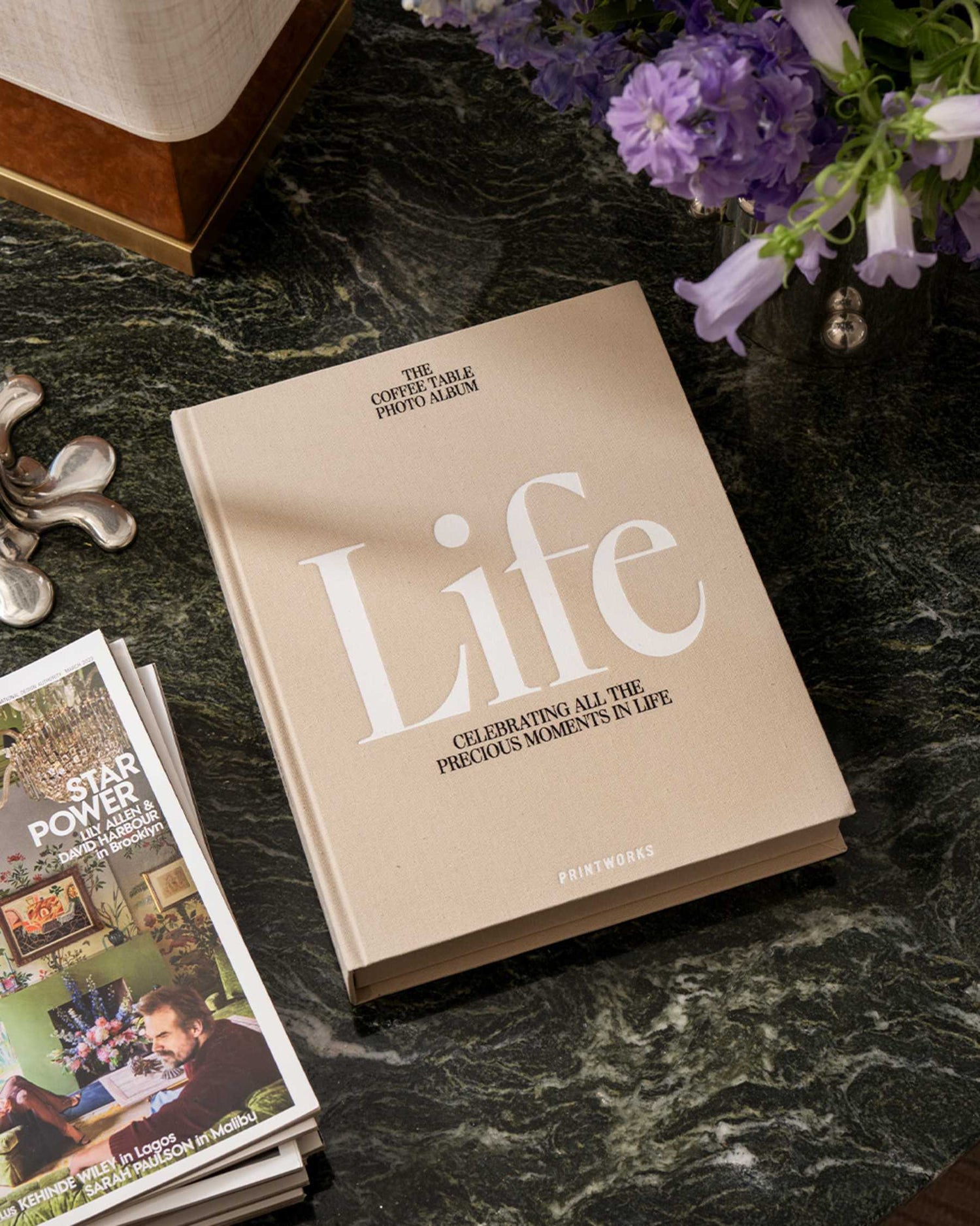 Photo album titled 'Life' on a marble surface with purple flowers and magazines.