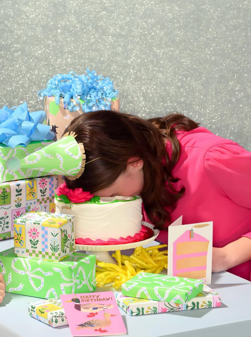 Person leaning over a table with decorative items including a cake, flowers, and greeting cards.