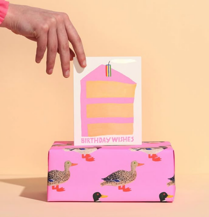 Pink gift box with duck designs and a 'Birthday Wishes' card on a beige background