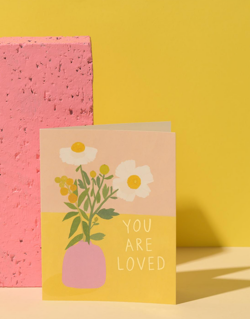 Greeting card with floral design and 'You are loved' text on a yellow background