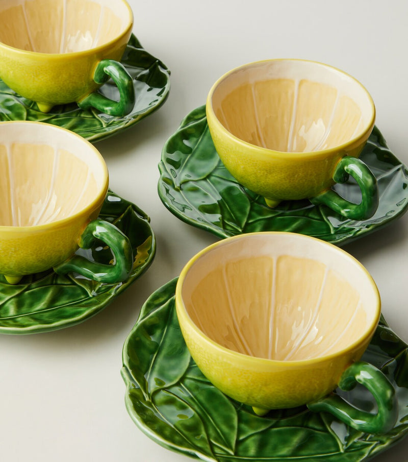 Set of four lemon-shaped ceramic cups with green leaf-like handles on matching plates.