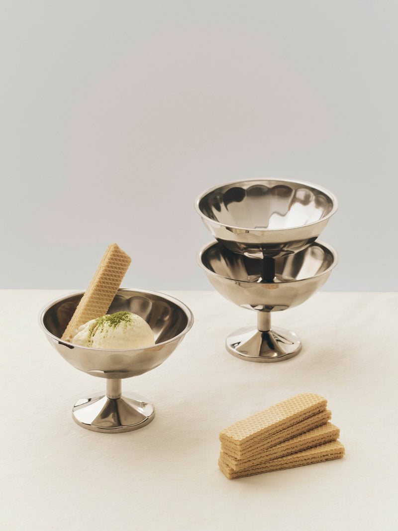Two silver ice cream bowls with a scoop of ice cream and wafers on a light background