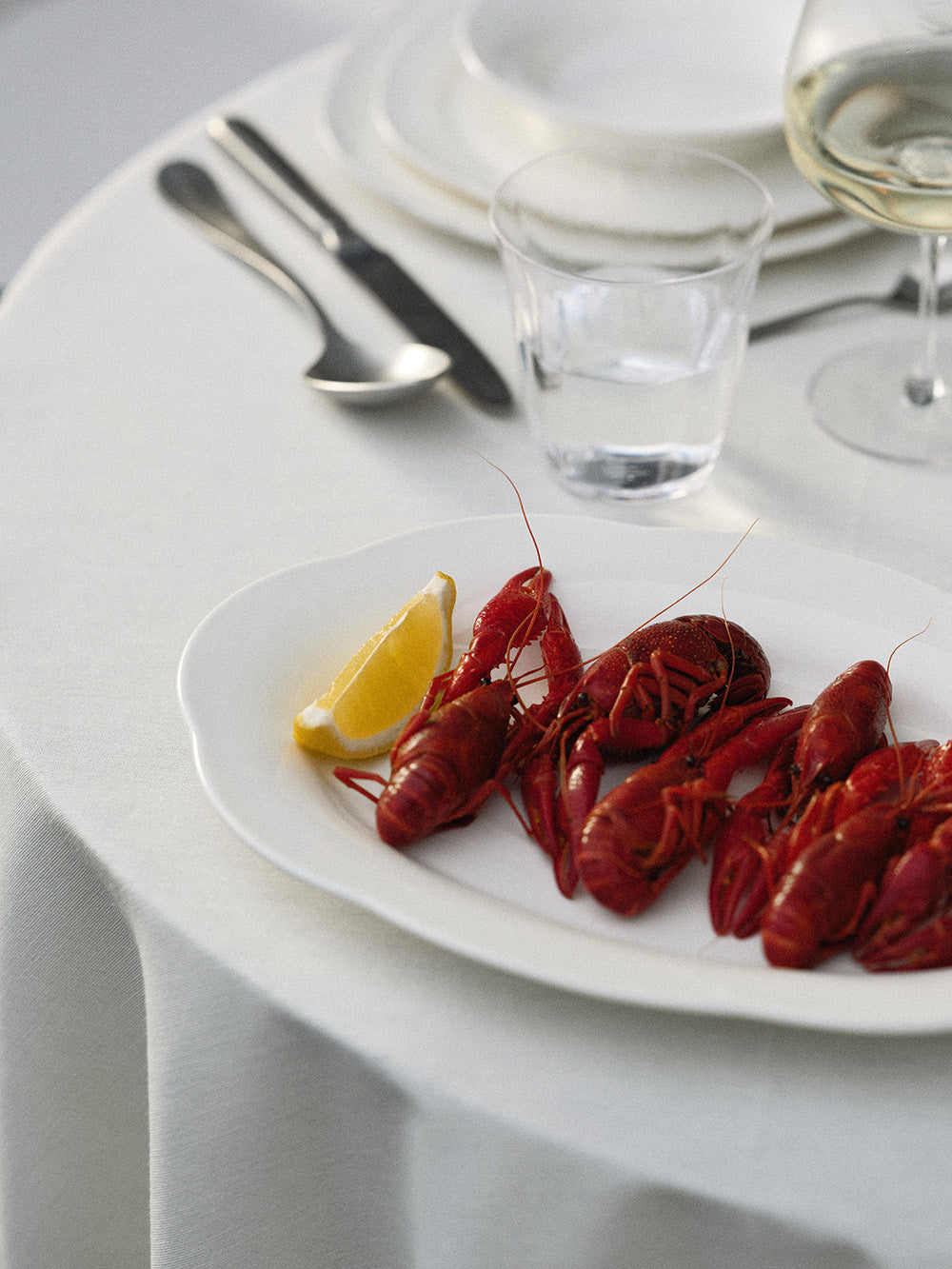 Plated crawfish with a lemon wedge on a white tablecloth with cutlery and glasses.
