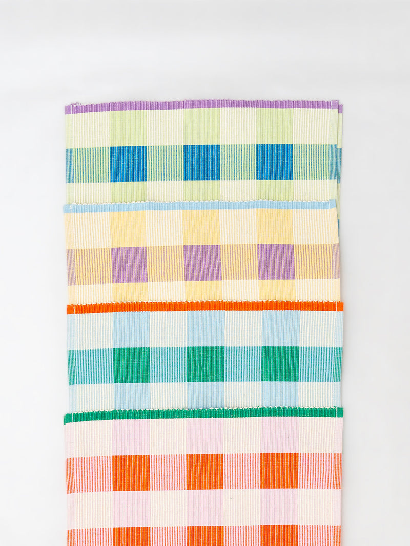 A set of woven placemats featuring a multicolor plaid and checkered pattern with stripes of purple, blue, yellow, green, orange, and pink on a white base, shown against a plain white background.
