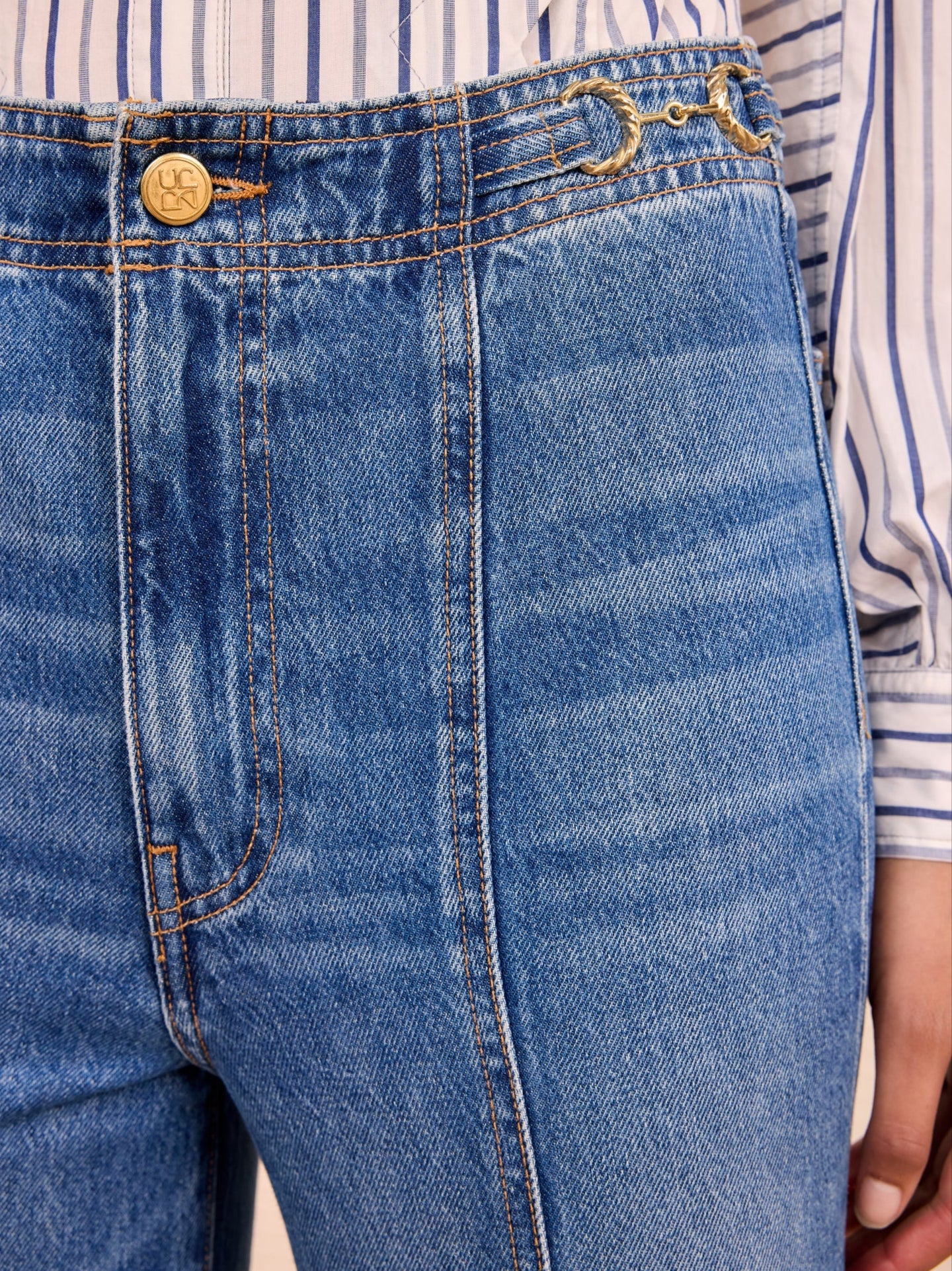Close-up of blue jeans with a striped shirt in the background