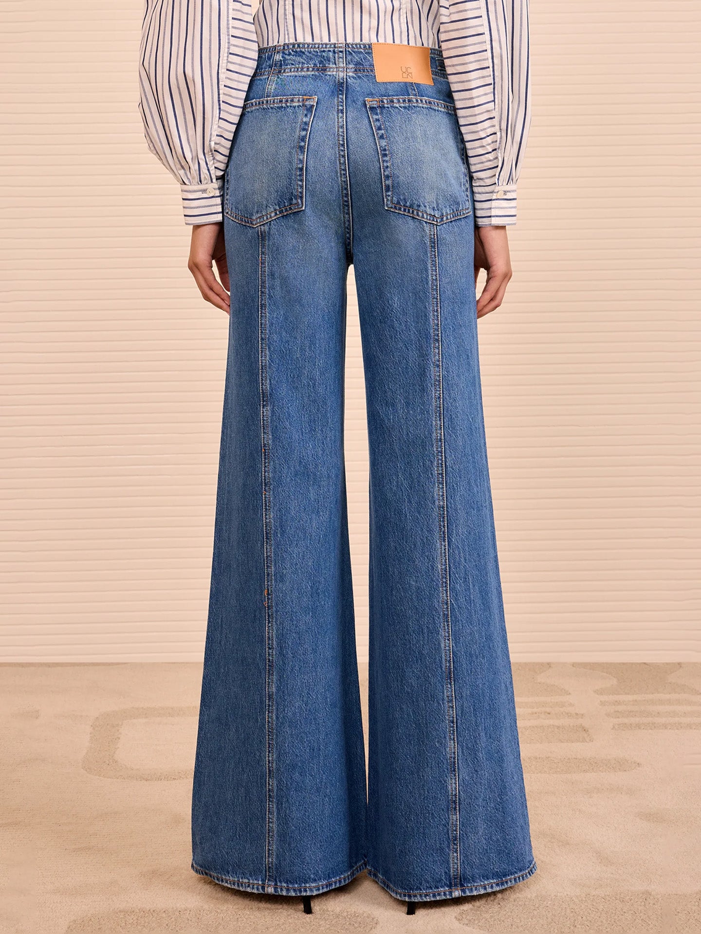 Person wearing blue wide-leg jeans and a striped shirt on a beige background