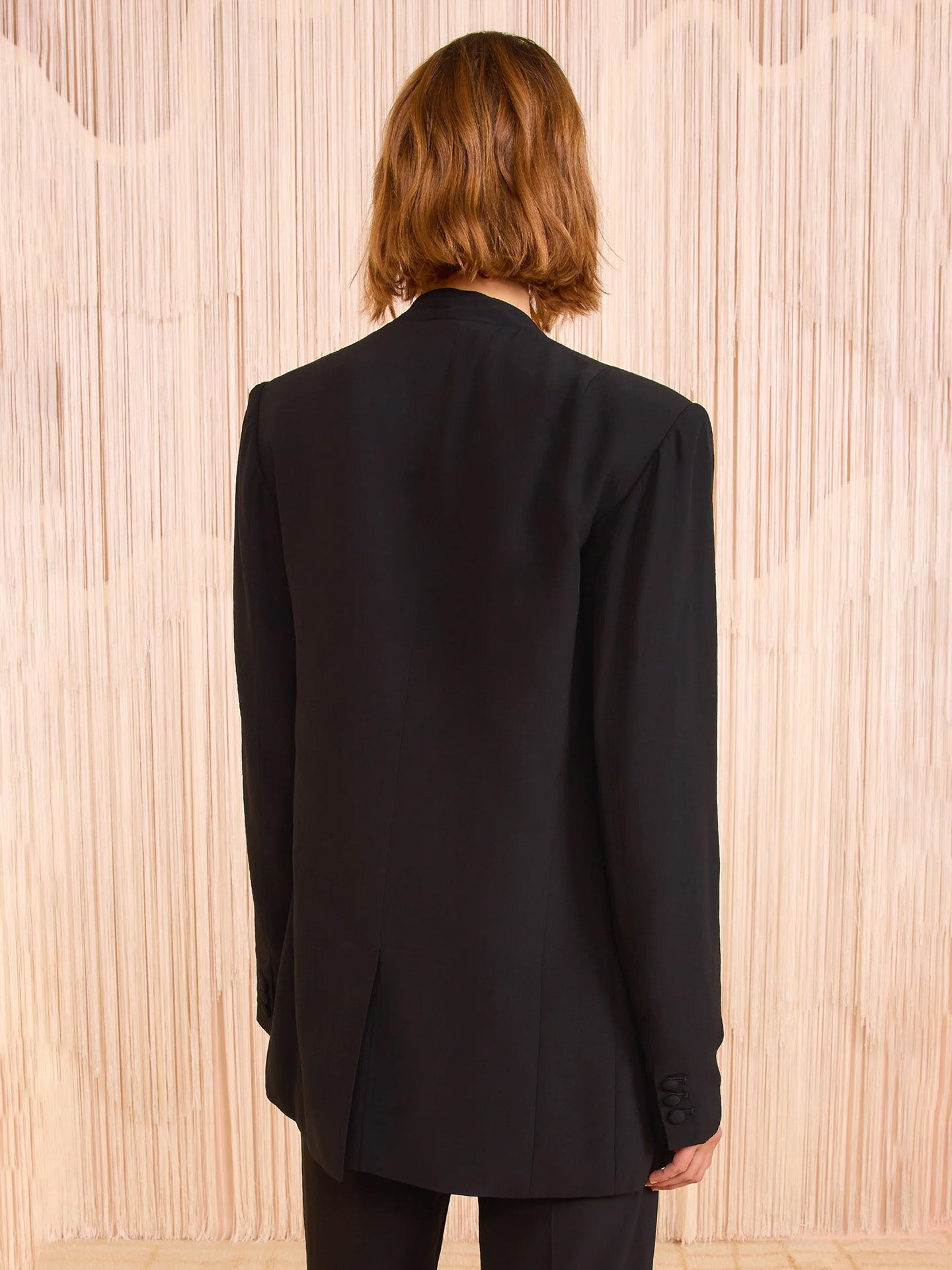 Person wearing a black blazer against a wooden paneled wall