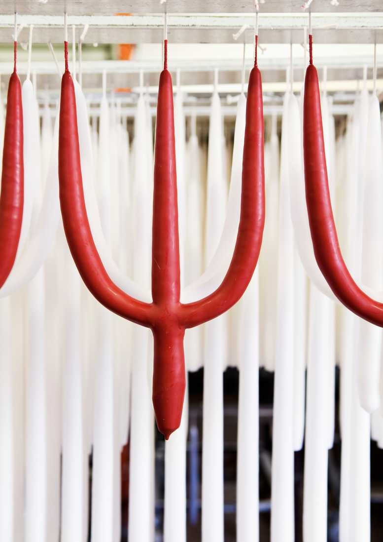 Red pitchfork shaped candle hanging in the candle factory against a white candles.