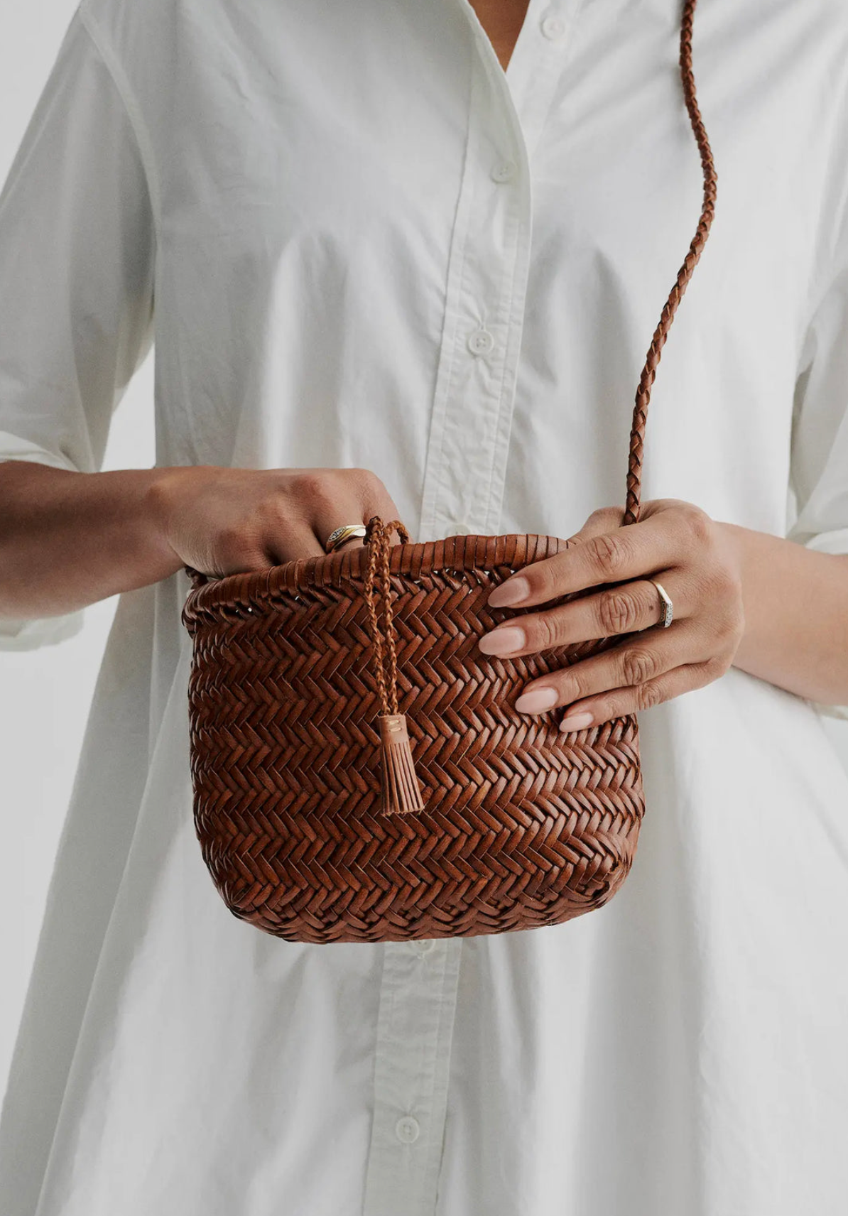 Person holding a woven brown handbag with a plain white background