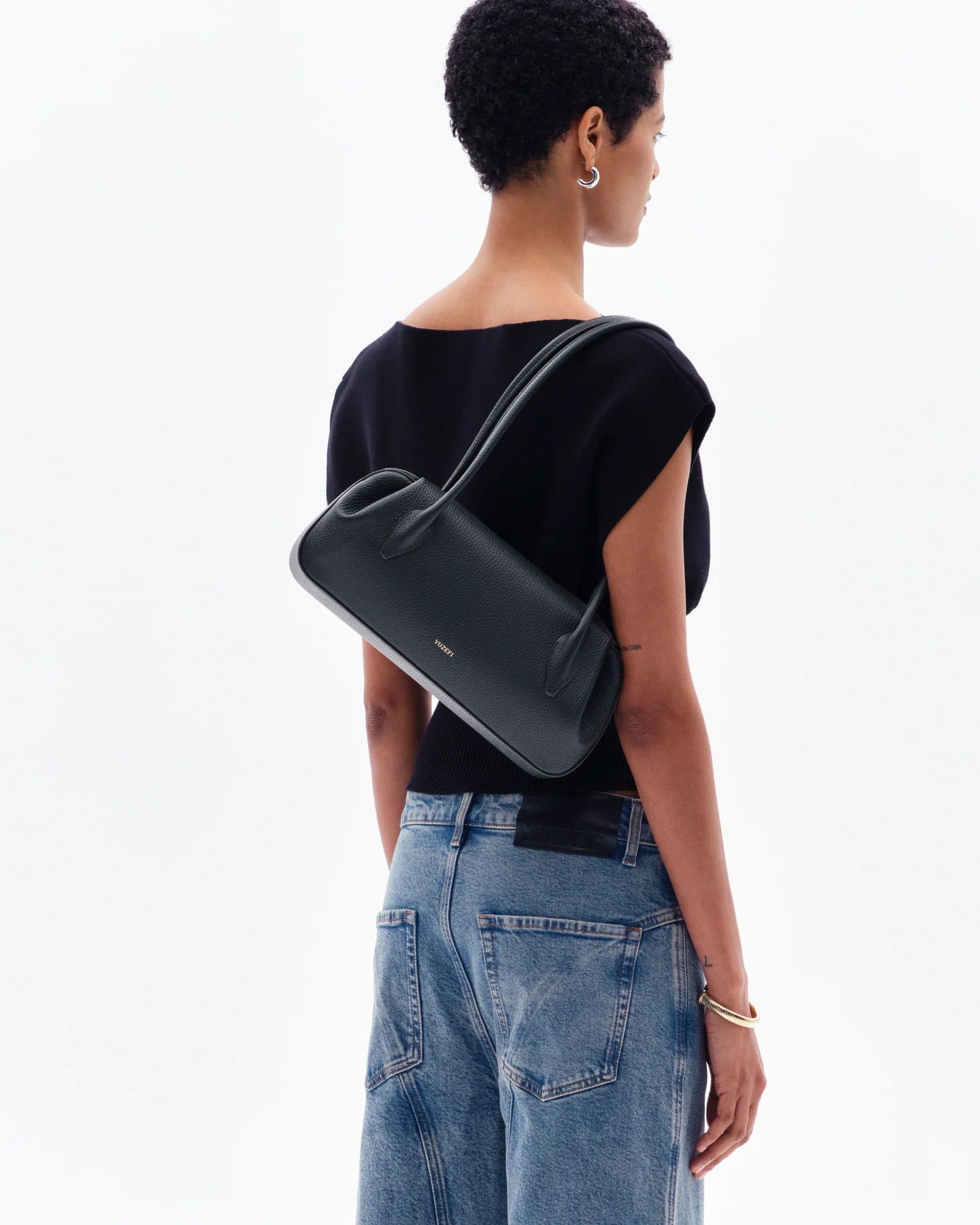 Woman wearing Yuzefi's black shoulder bag on a white background