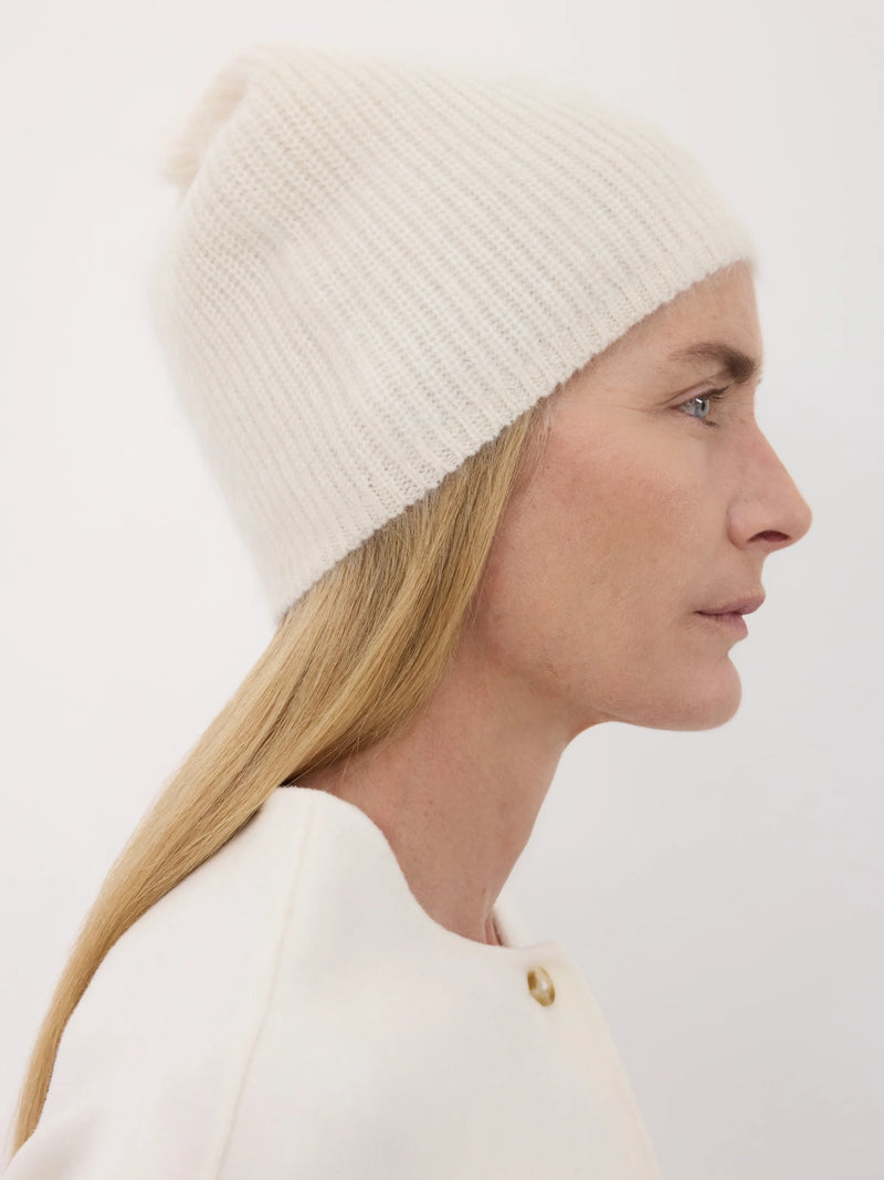 Woman wearing an ivory knit beanie and white top against a plain background