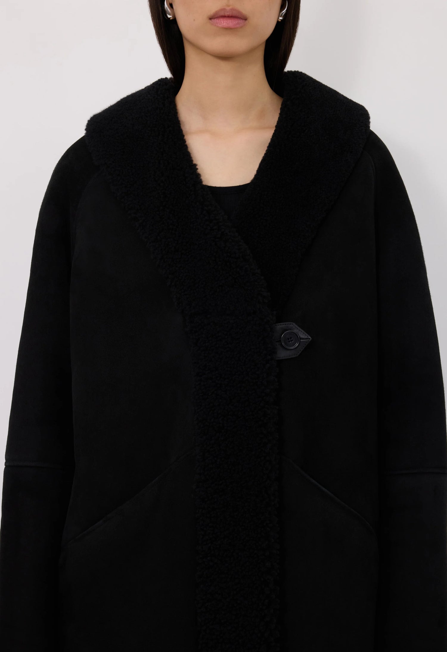 Black shearling coat worn by a person on a white background