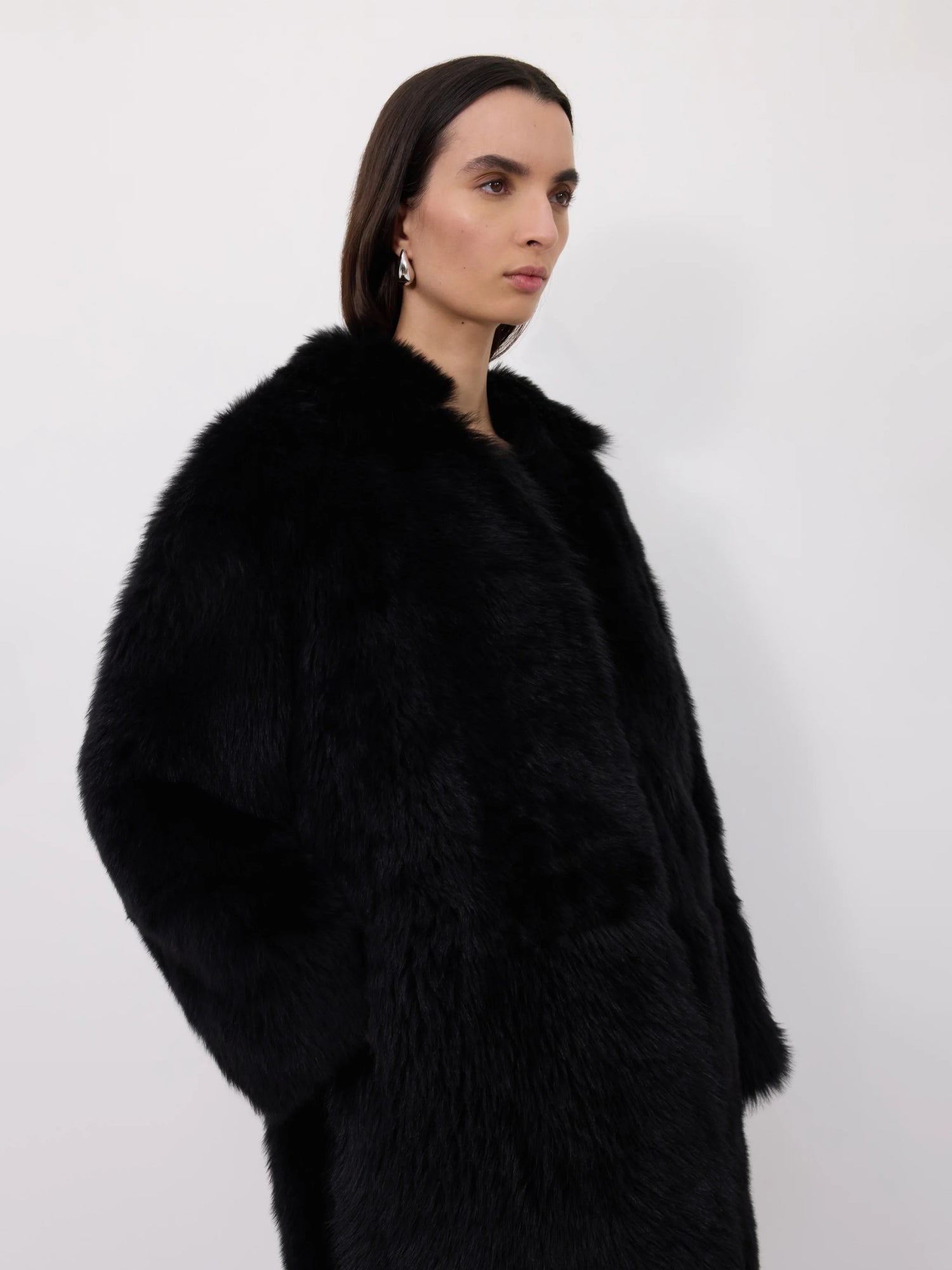 Woman wearing a black shearling fur coat against a white background