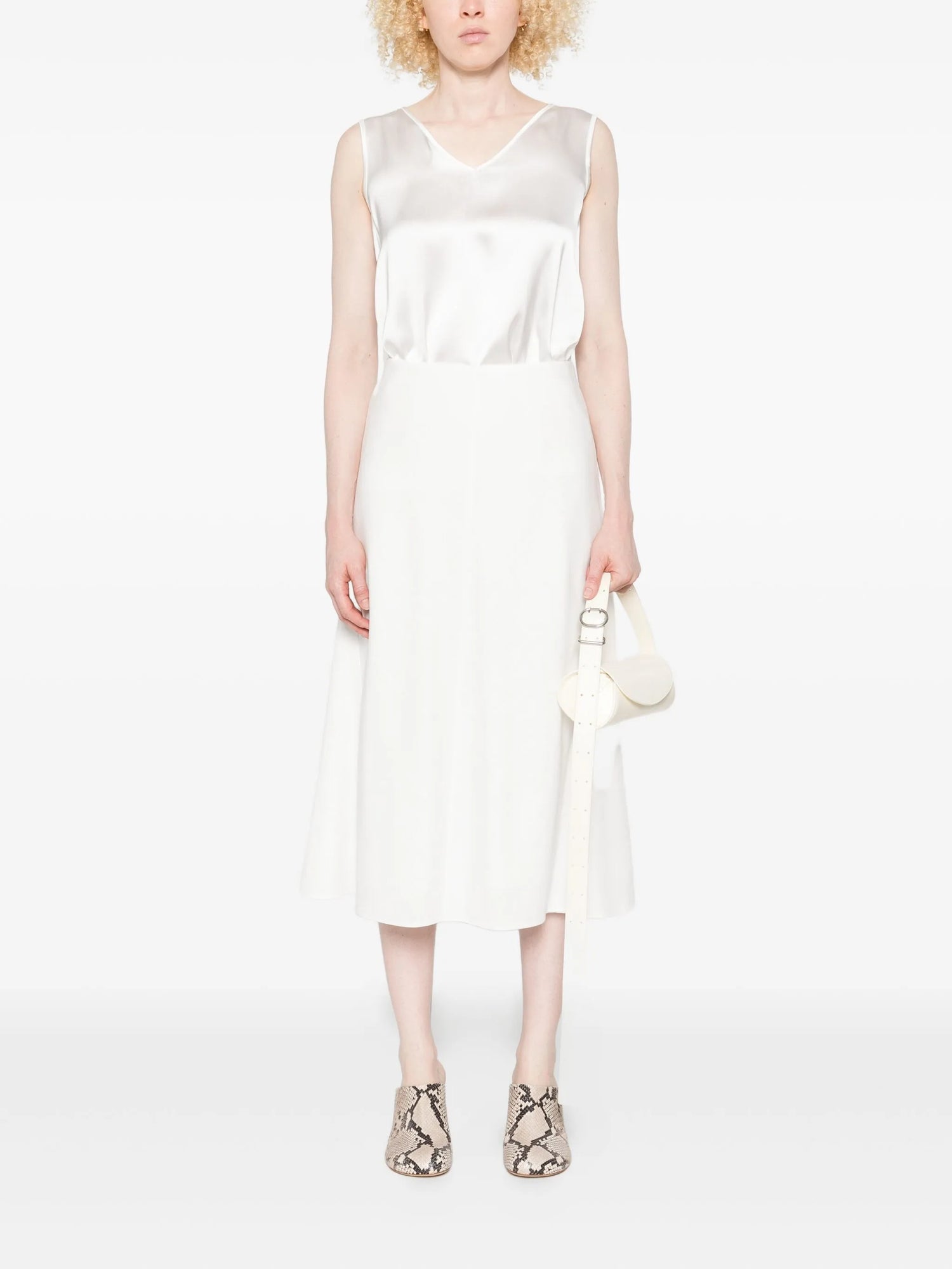 Woman wearing a white sleeveless dress holding a matching handbag on a white background