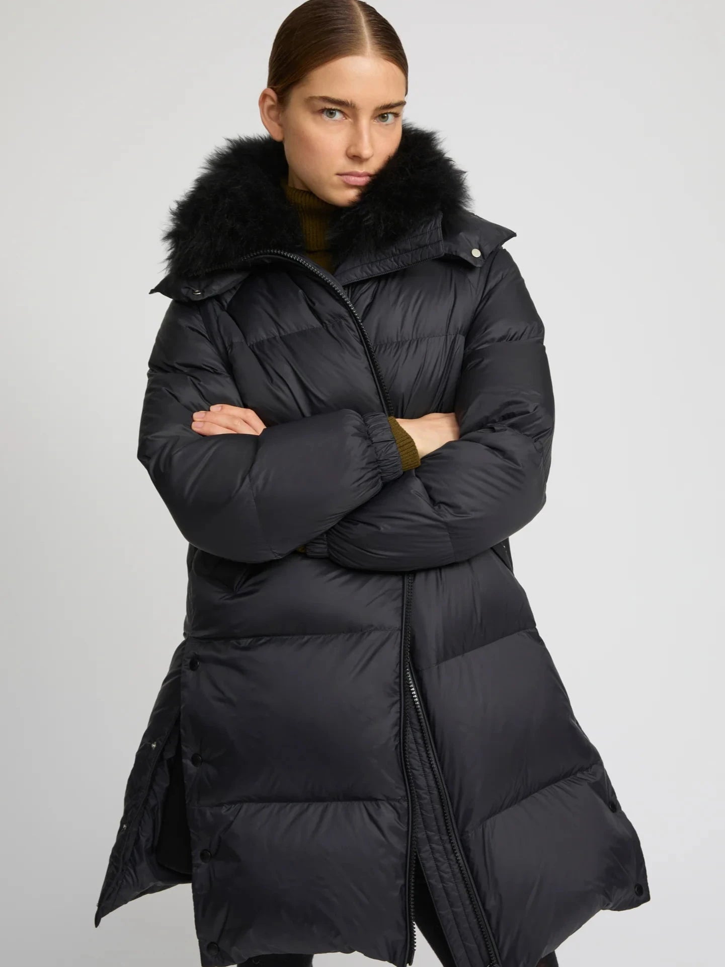 Model wearing a black puffer coat with fur hood on a gray background