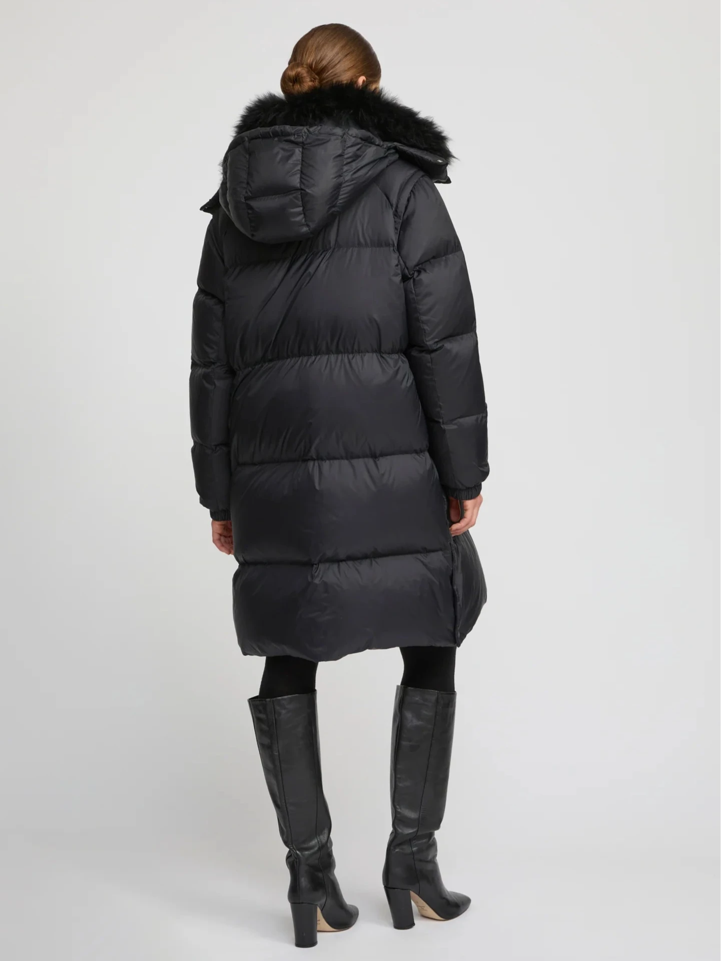 Person wearing a black puffer coat with fur hood on a white background