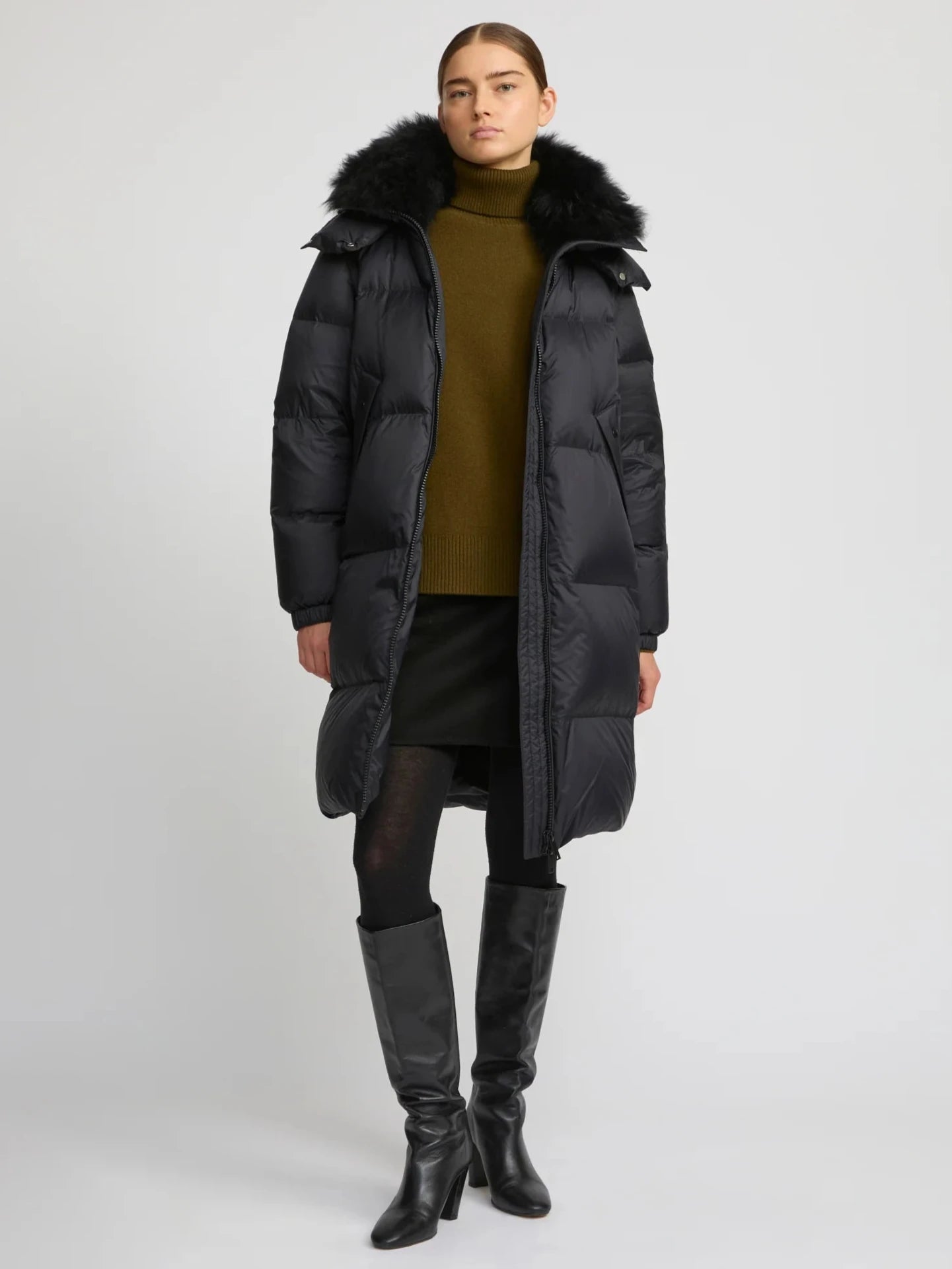 Person wearing a long black coat with fur hood on a white background