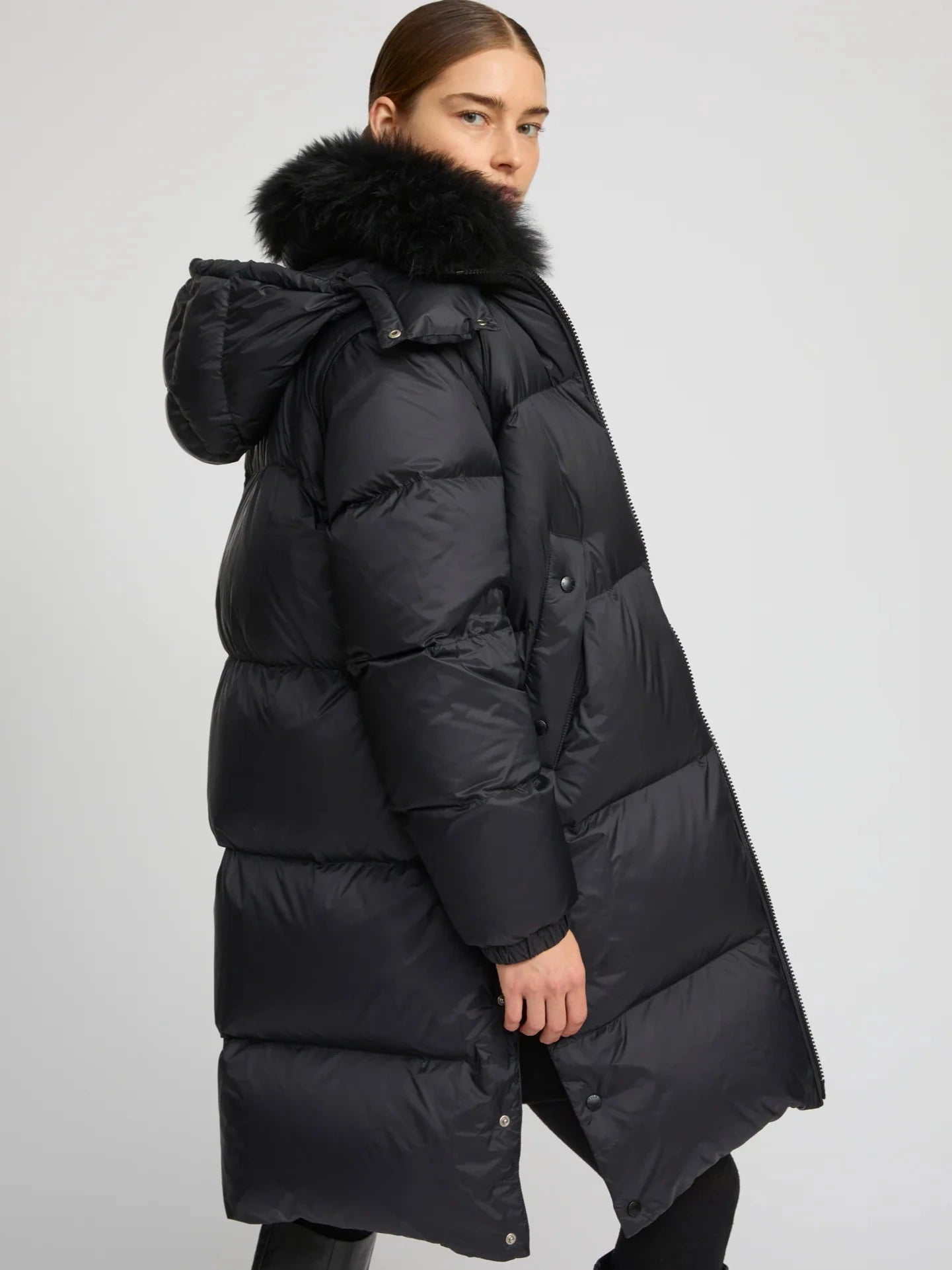 Person wearing a long black puffer coat with a fur-lined hood on a light gray background