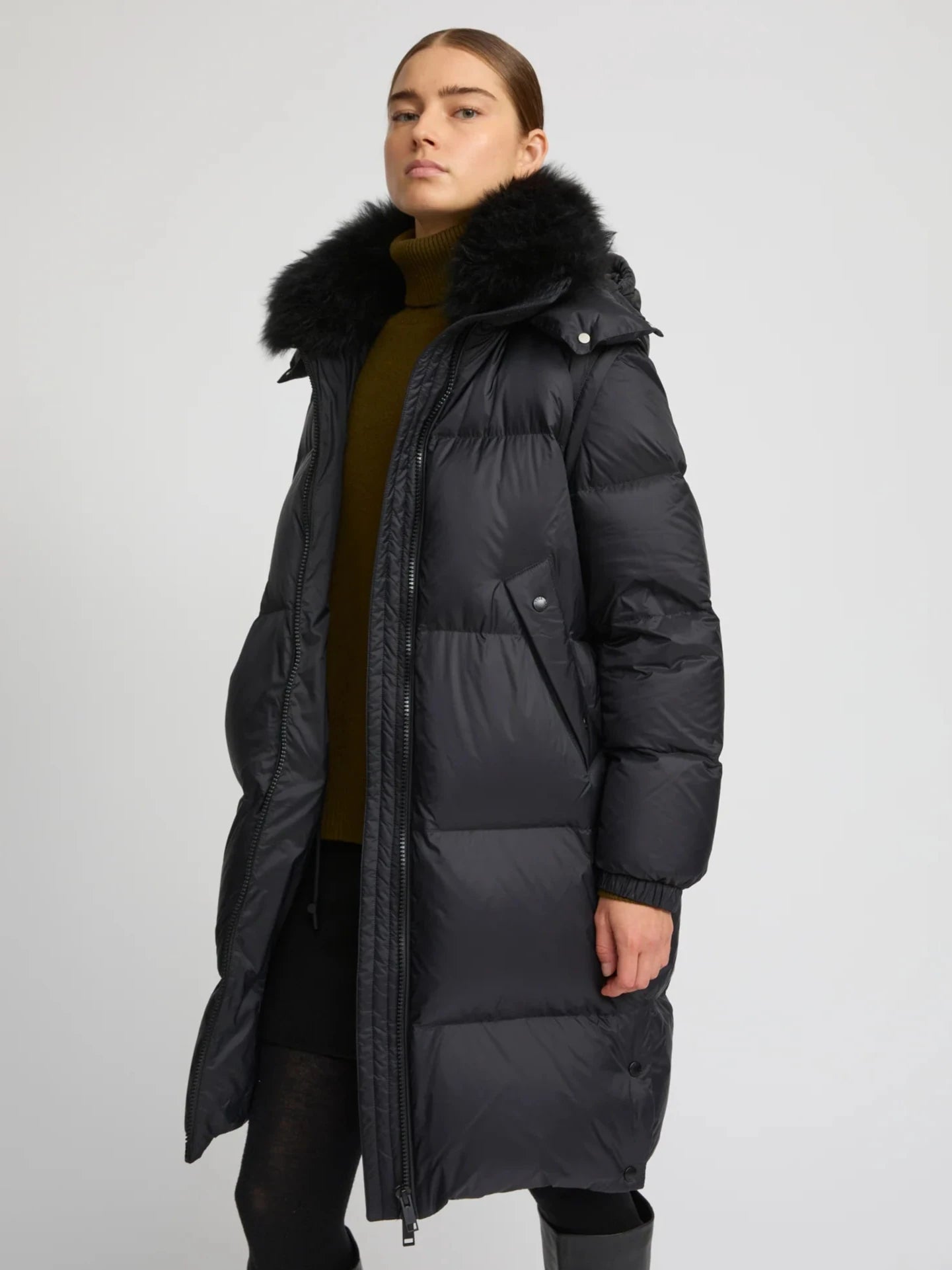 Person wearing a black puffer coat with a fur-lined hood on a light gray background
