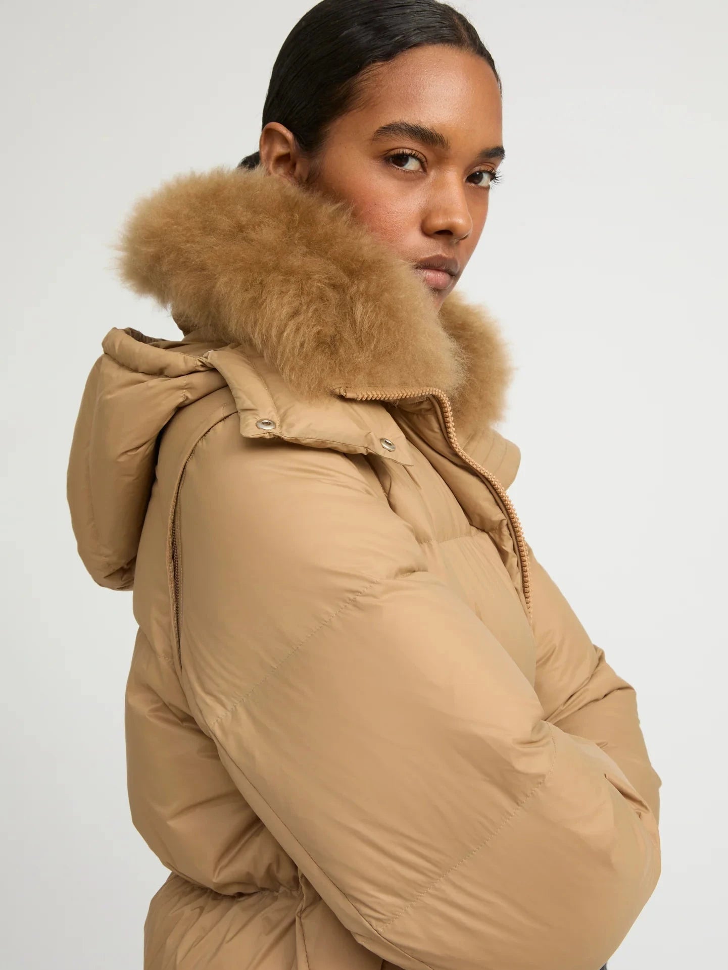 Woman wearing a beige puffer jacket with a fur hood on a white background
