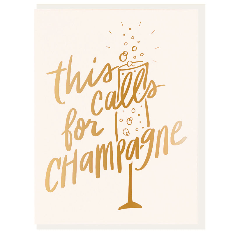 A folded greeting card with the text 'This Calls for Champagne' printed in gold foil on the front, accompanied by an illustration of a champagne glass with bubbles.