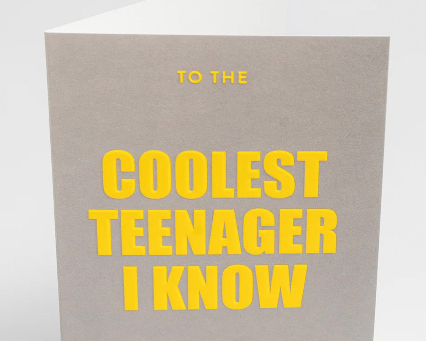 A greeting card with the text To the coolest teenager I know standing with yellow thick font on grey