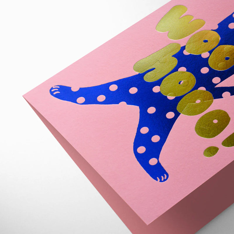 Card with blue polka-dotted cat and gold text on pink background
