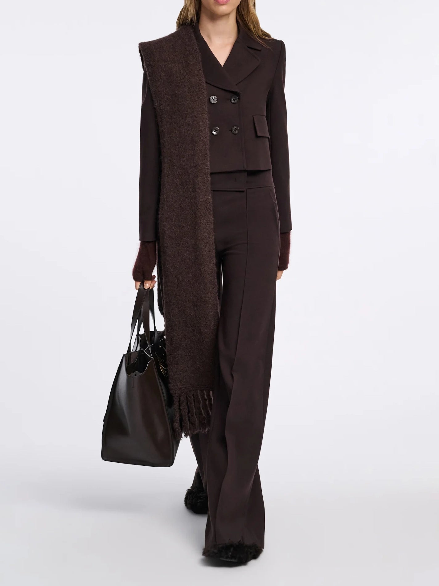 Woman wearing a brown suit with a long vest holding a black handbag on a white background