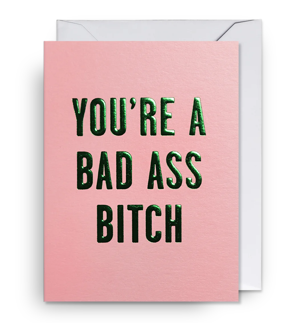 A pink mini greeting card with the text 'YOU'RE A BAD ASS BITCH' in green capital letters, accompanied by a white envelope.