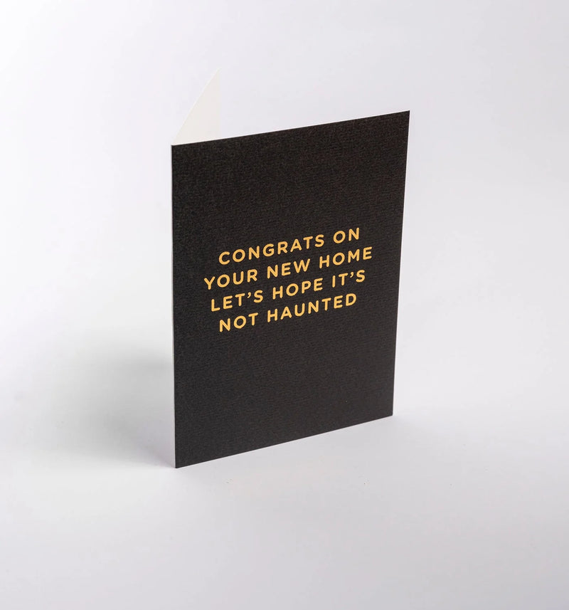 Black card with gold text 'Congrats on your new home, let's hope it's not haunted' on a white background