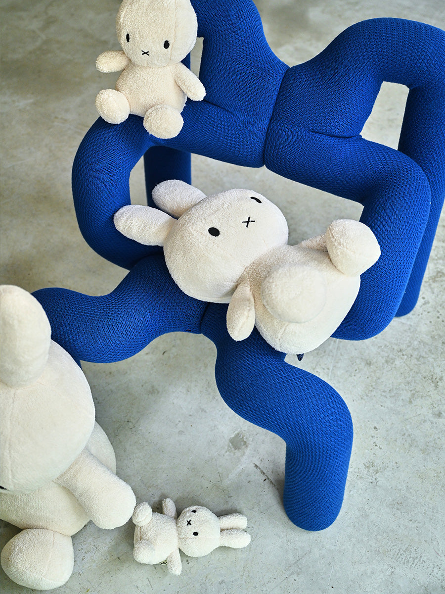 White plush toys on a blue wavy chair against a concrete floor.