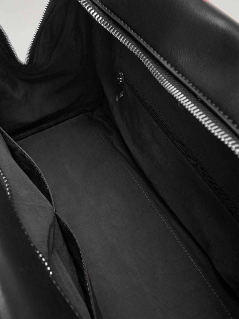 Close-up of a black leather bag's inside lining, showing the zipper closure and inside pocket with a hidden zipper and two other pockets that have no closures.