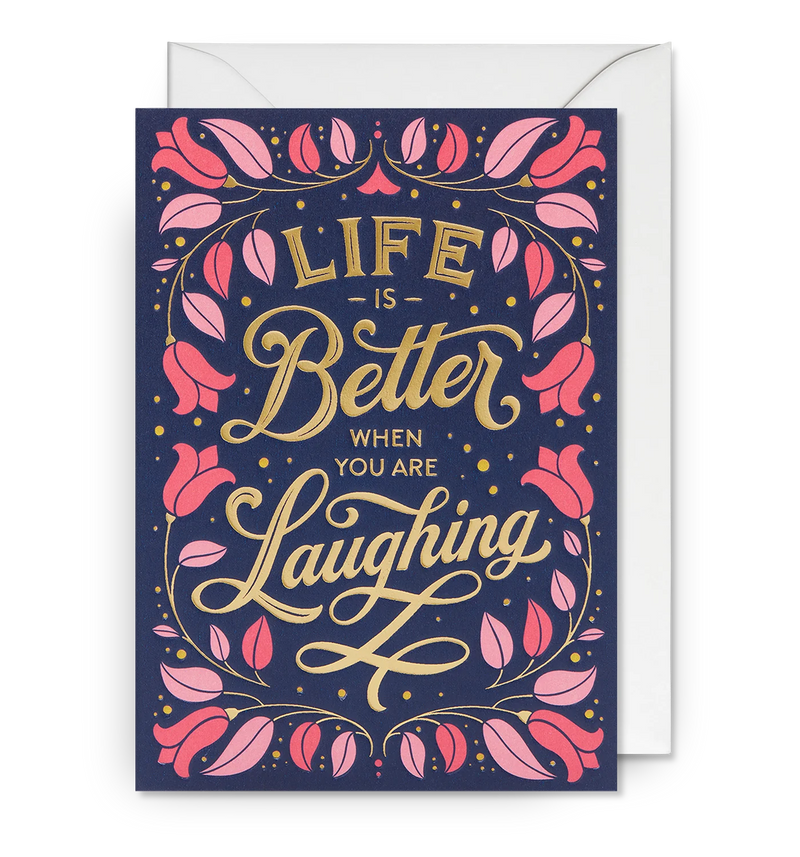 Greeting card with the phrase 'LIFE IS BETTER WHEN YOU ARE LAUGHING' surrounded by floral designs, in gold color on a navy background, accompanied by a white envelope.