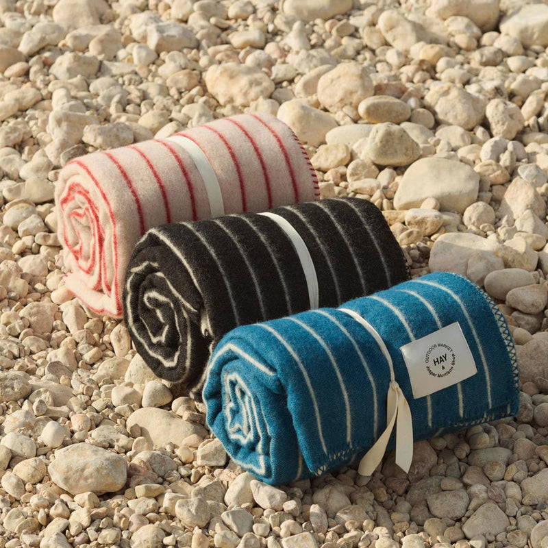 Three rolled-up wool throws with striped patterns on a pebbly surface