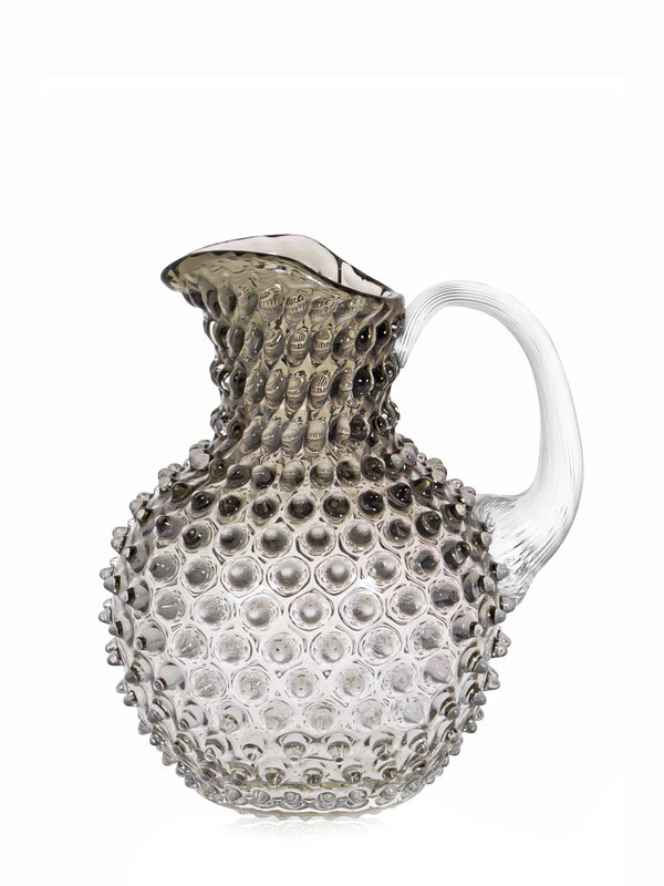 A beige-colored glass jug with a traditional hobnail pattern, featuring a textured surface and a white handle.