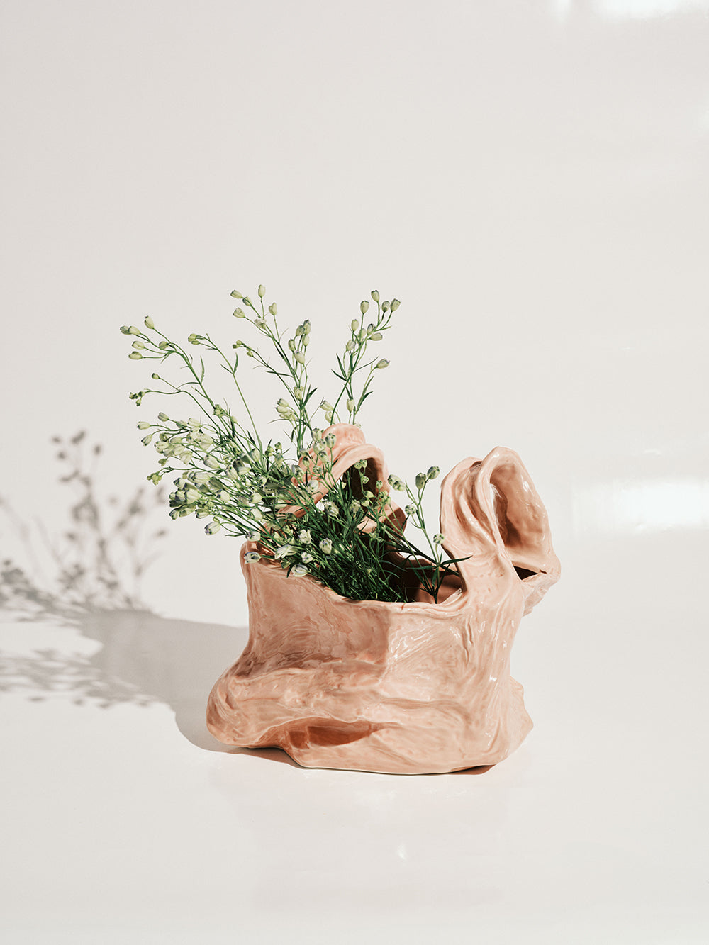 Ceramic bag vase with plants on a light background