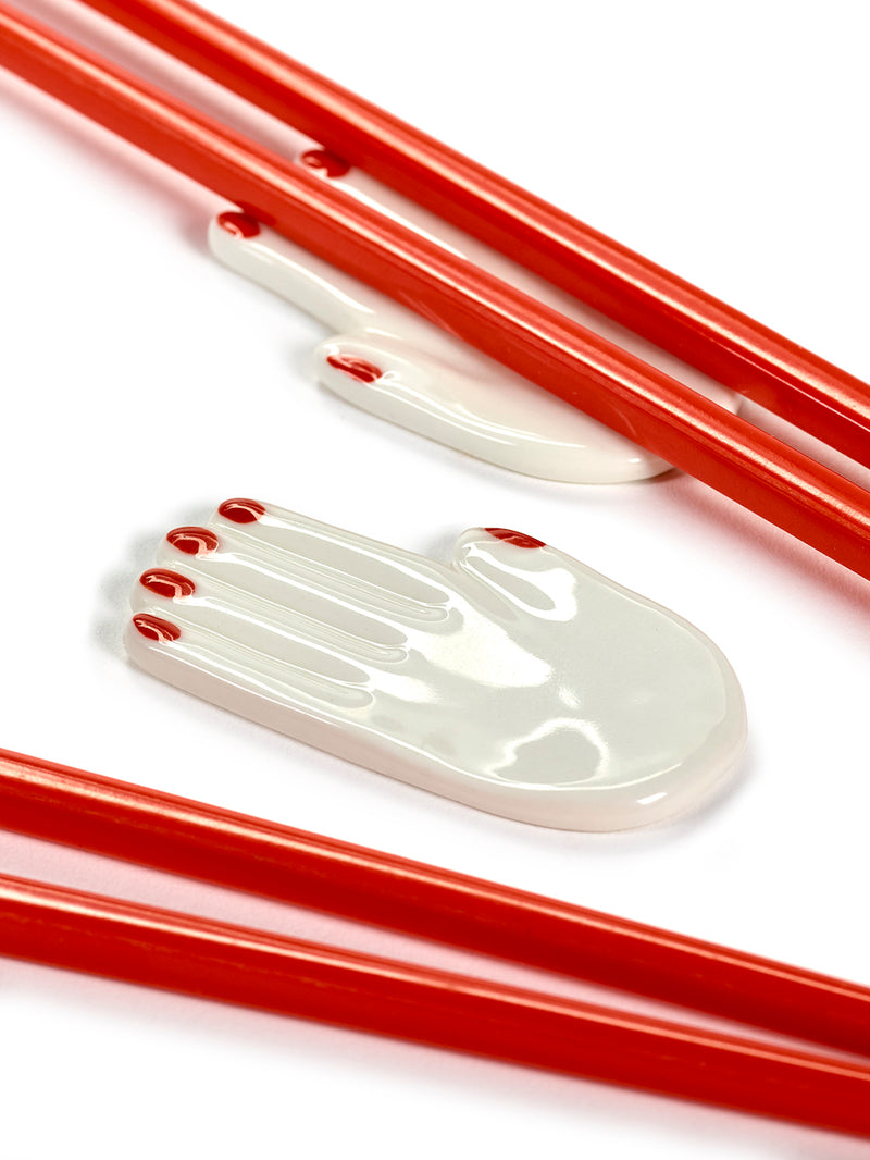 Red chopsticks with white ceramic hand-shaped objects on a white background
