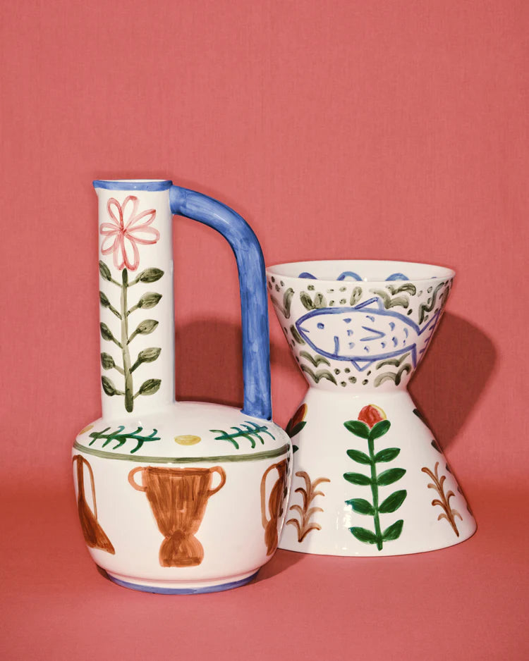 Two ceramic pitchers with floral and fish designs on a pink background