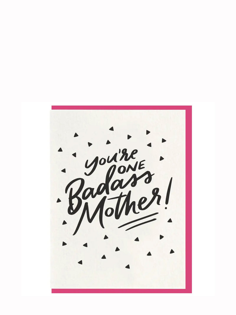 A greeting card with 'You're One Badass Mother!' written in stylized black lettering on a white background, with a pink envelope.